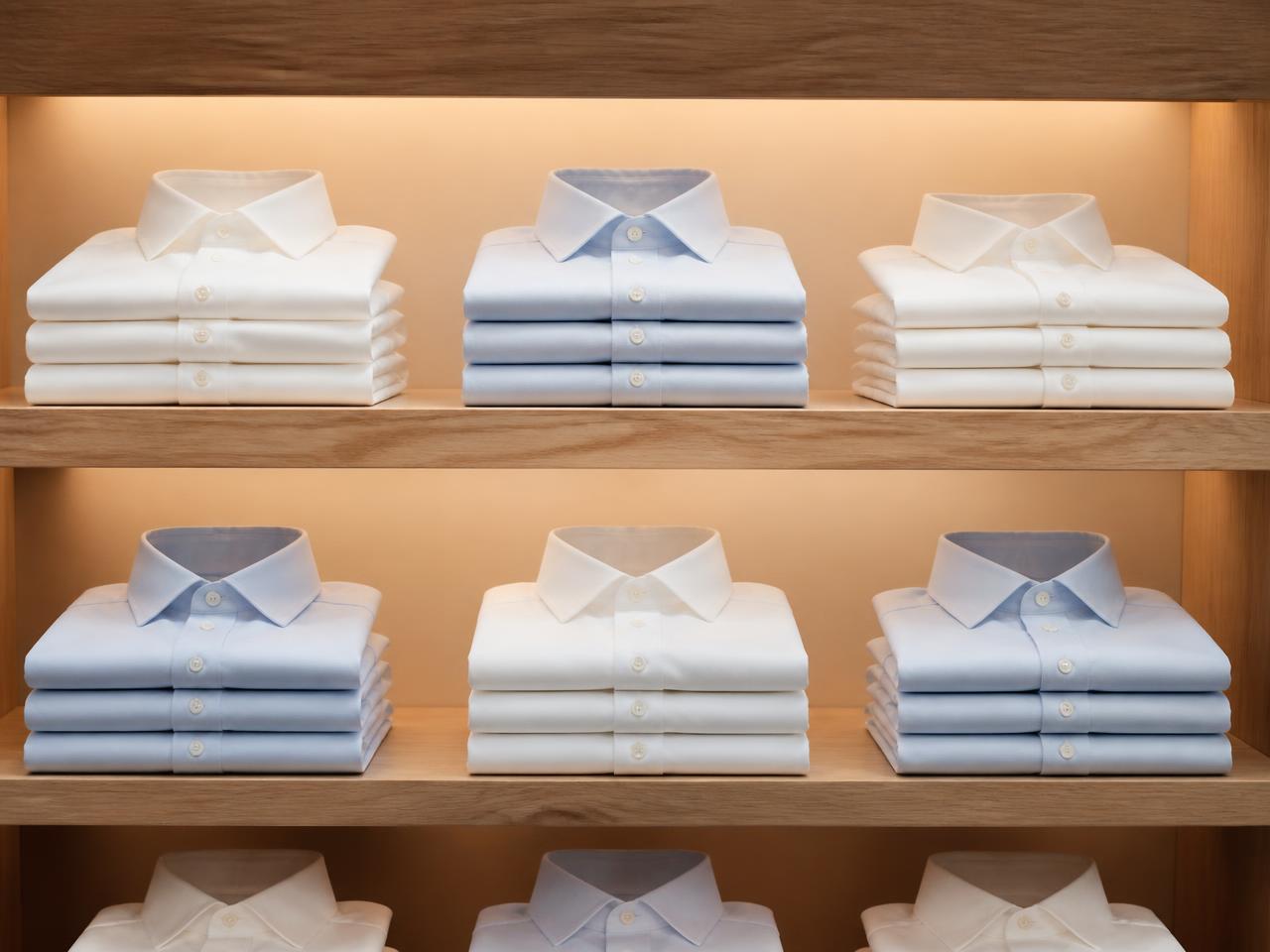Folded custom white and blue shirts on lit oak shelving